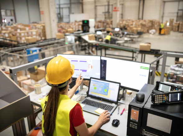 A woman is analyzing real-time data on her computer within a warehouse, demonstrating tech integration in logistics.